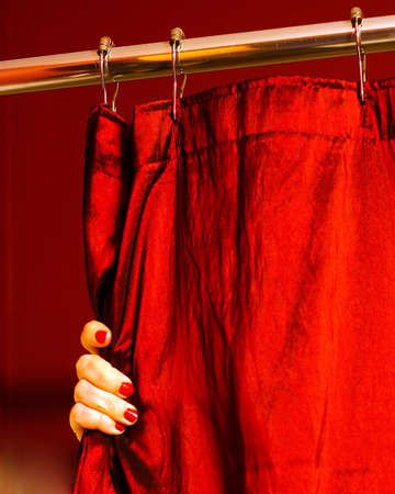 A portrait photograph of a woman's hand with painted finger nails holding a red shower curtain.  The metallic curtain could be held either open or closed by the hand.の写真素材