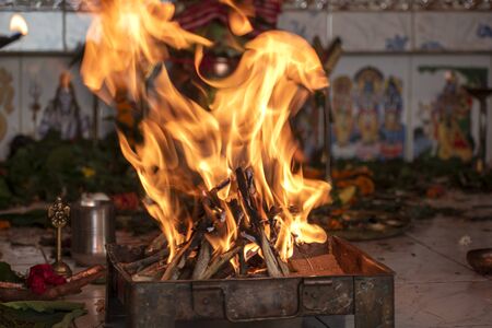 Panditji doing the Havan or yagna pooja. A pooja thali with some lamp, flower, coconut, copper pot, incense sticks, betel leaf, and camphor and the fire in the decorated clay or copper pot.の写真素材