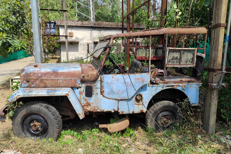 Weathered by time, a vintage jeep or van left in a neglected condition rests under the sun, embraced by nature. Rust and peeling blue paint hint at past adventures.の写真素材