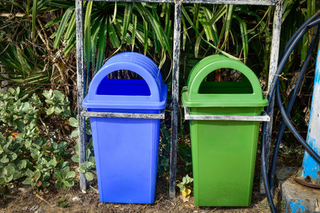 Two cheerful bins, blue and green, sit under lush green leaves. Locked to a steel frame, they add...