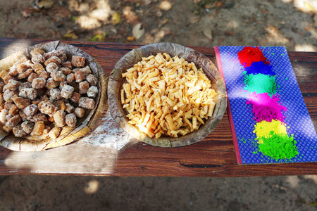 Top view of Indian Holi snacks served in eco-friendly leaf bowls alongside bright Holi colour gulal powder on a rustic wooden tableâconcept of the Indian festival of colours, culture, and celebration.の写真素材