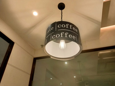 Modern pendant lamp with coffee typography hanging from the ceiling in a contemporary cafÃ© interior. Warm lighting creates an inviting atmosphere, which is ideal for a coffee shop and interior design.の写真素材