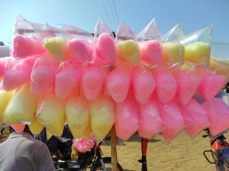 Colourful cotton candy is showcased in clear plastic bags at an outdoor market. Evoking childhood treats and street food culture, perfect for themes of dessert, fun, carnival, and local market life.の写真素材