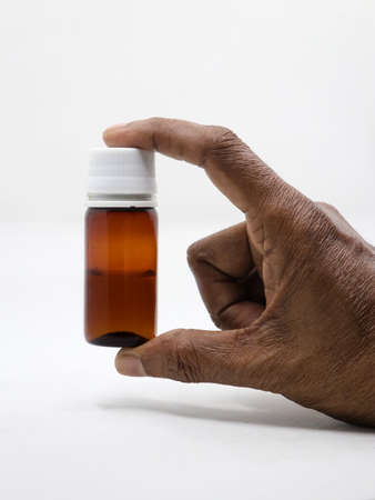 a bottle of medical test sample for testing in hospital laboratories held between fingers of hand of a person isolated in a white backgroundの写真素材