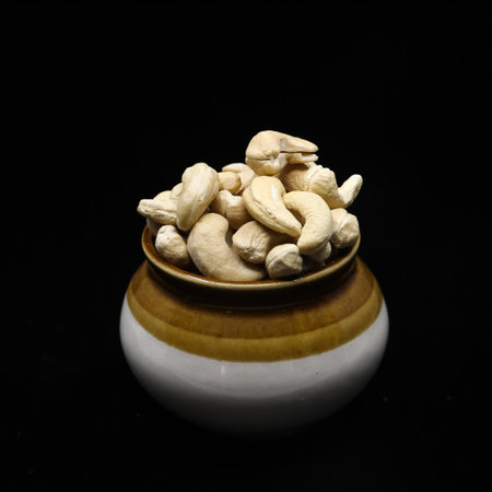 closeup shot of fresh cashew nuts filled up and stored in a traditional pot jar isolated in a black backgroundの写真素材