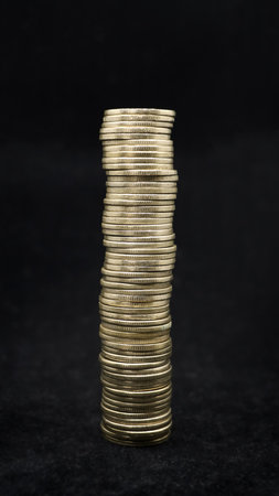 shiny gold coins stacked up and arranged to form a tall tower isolated in a black backgroundの写真素材