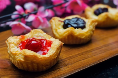Open mini pies with berries  jams on wooden plate