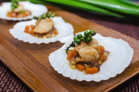 Seared scallops  served on a bed of vegetables, presented on a scallop shell, on wooden plateの写真素材