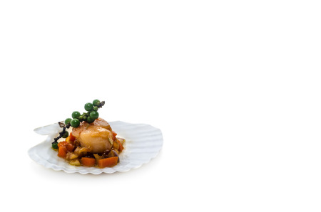 Seared scallops with vegetables, presented on a scallop shell, isolated on white background.