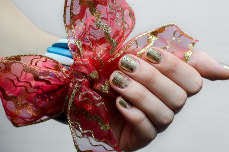Female hand with gold nail design and red bow. Skin and nail care.の写真素材