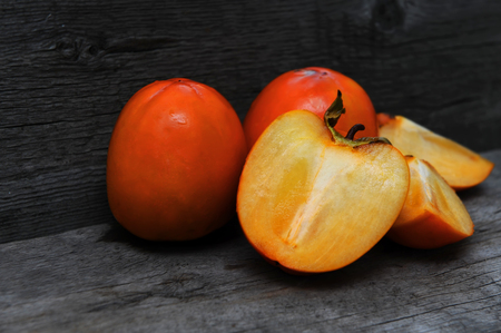 Three delicious orange persimmons on wooden background.の写真素材