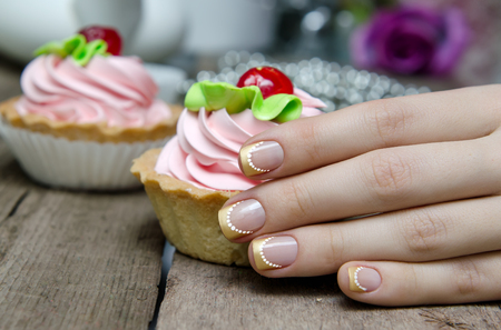 Woman hand with gold french manicure hold sweet cupcake.の写真素材