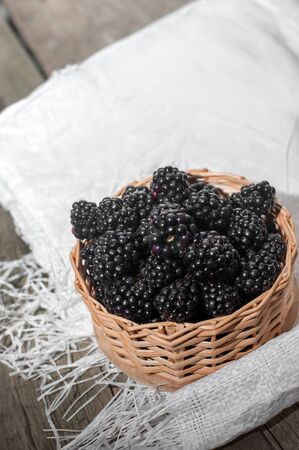 Blackberries in a small wicker basket on wooden table.の写真素材