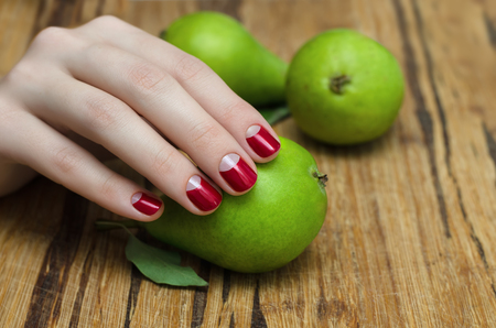 Woman's hand with red manicure holding fresh green pear.の写真素材