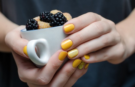 Female hand with yellow nail design holding a cup with berriesの写真素材