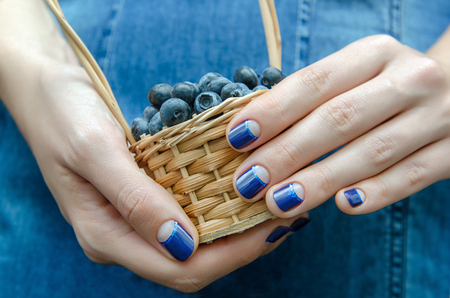 Female hand with blue nail design holding a small basket with berriesの写真素材