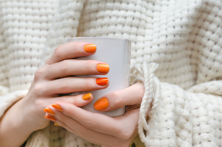 Female hands with orange nail design holding white cup.の写真素材