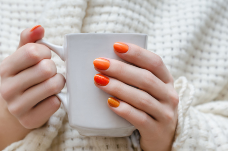 Female hands with orange nail design holding white cup.の写真素材