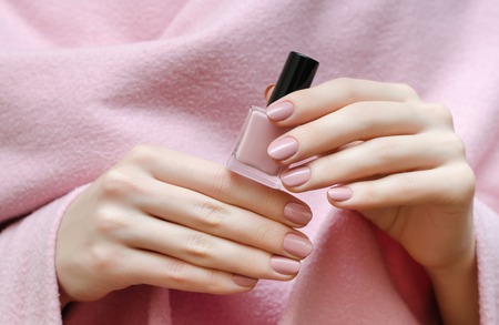 Beautiful female hand with warm pink nail design holding nail lacquer bottle.の写真素材