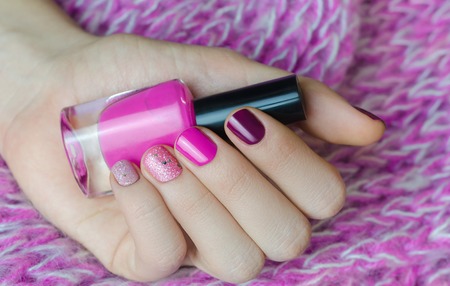 Nail art with glitter. Beautiful female hand with pink manicure holding nail lacquer bottle.の写真素材