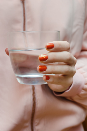 Nail art with glitter. Beautiful female hand with orange manicure holding glass of water.の写真素材