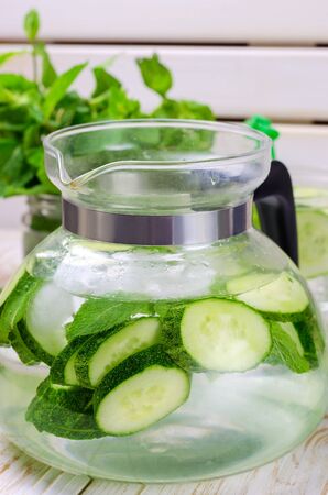 Fresh water with cucumber, mint and ice in glass jugful on wooden table, closeup.の写真素材