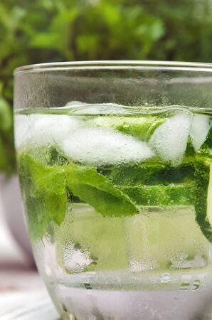 Fresh water with cucumber, mint and ice in glassware on wooden table, closeup.の写真素材