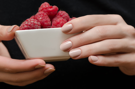 Female hands with beige manicure holding white bowl with raspberry.の写真素材