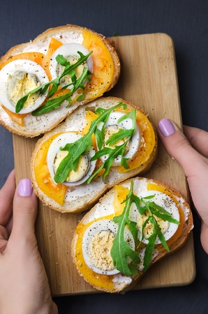 Sandwiches with boiled eggs, yellow tomatoes and arugula on wooden cutting board.の写真素材