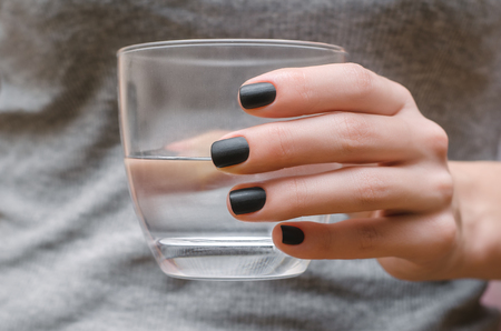 Female hands with black matte nail design holding glass of water.の写真素材