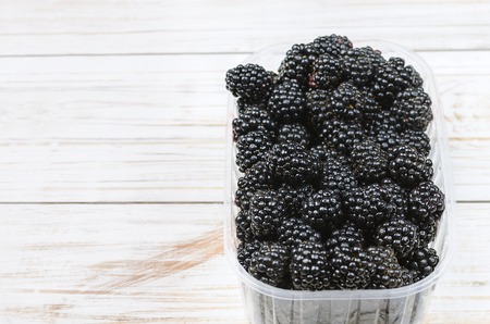 Box with blackberries in female hands on wooden background.