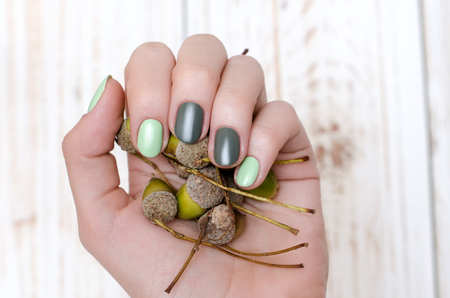 Female hands with beautiful green nail design holding green acorns.の写真素材