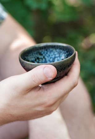 Tea bowl in men's hand, closeup. Tea ceremony outdoors.