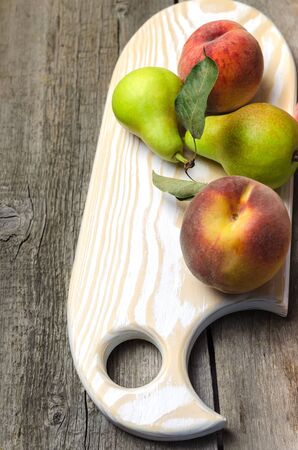 Fresh pears and peaches on white wooden cutting board.の写真素材