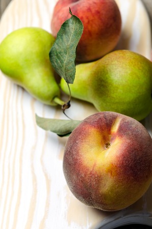 Fresh pears and peaches on white wooden cutting board.の写真素材