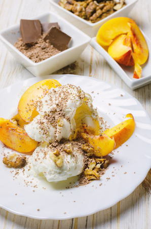 Ice cream with peach, chocolate and nuts on white plate.の写真素材