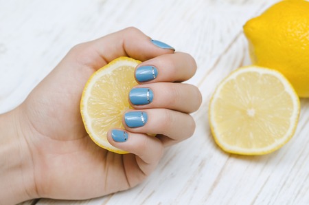 Female hands with light blue nail art holding a piece of lemon.の写真素材