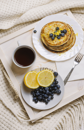 Pancakes with blueberry and cap of coffee on a wooden tray on a bed. Nice breakfast.の写真素材