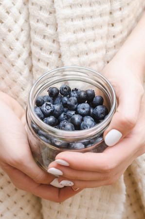 Blueberry in glass jar in female hands. Vertical format.の写真素材
