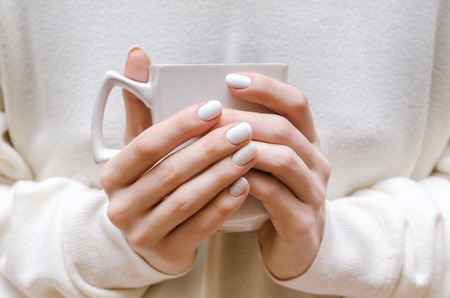 Female hands with white nail design holding white cup.の写真素材