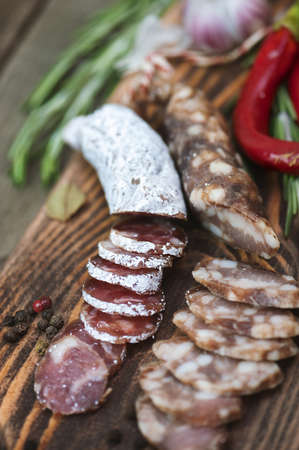 Sliced salami with rosemary and chili pepper on wooden cutting board.の写真素材