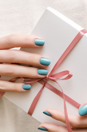 Female hands with turquoise manicure holding white gift box.の写真素材