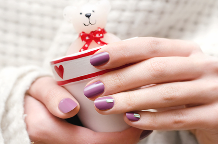 Female hands with purple nail design holding romantic candle.の写真素材