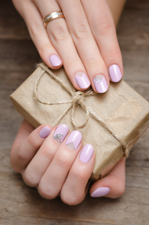 Female hands with light pink nail design holding a present box.の写真素材
