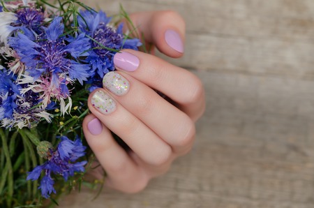 Female hands with pink nail design holding blue flowers.の写真素材