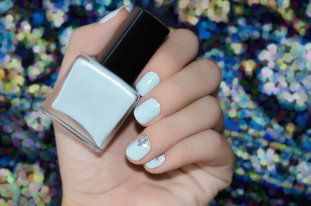 Female hand with blue nail design holding nail polish bottleの写真素材