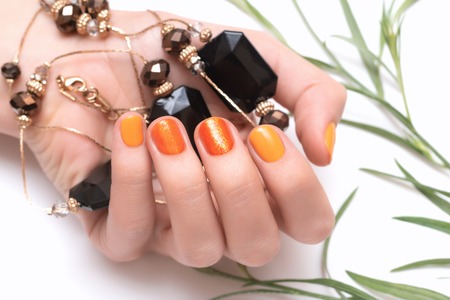Female hand with orange nail design on white background.の写真素材
