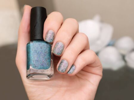 Female hand with thermal blue nail design holding nail polish bottleの写真素材