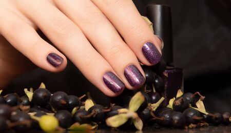 Female hand with purple nail design holding nail polish bottleの写真素材