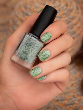 Female hand with green nail design holding nail polish bottleの写真素材